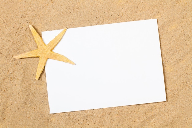 A yellow starfish with a blank white paper on the sand with copy space