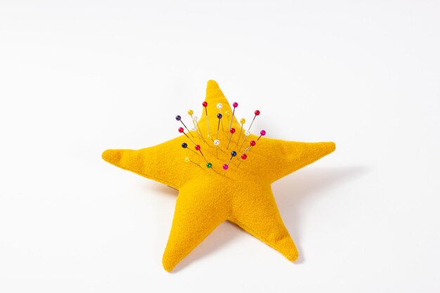 Photo yellow starshaped pincushion with colored pins pinned on a white background