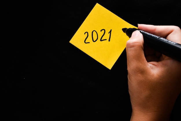 Photo yellow sticker with the symbol 2021 and a hand holds a marker.