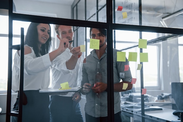 Yellow stickers is on the glass. Young business people in formal clothes working in the office.