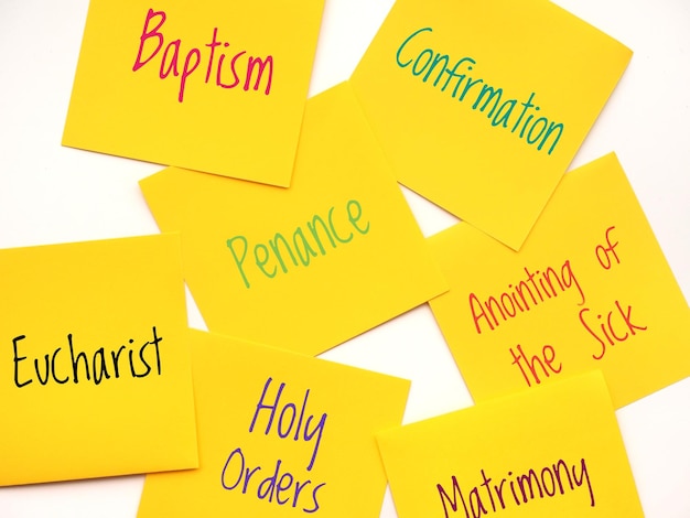 Foto note adesive gialle con i sette sacramenti, note di carta sullo sfondo con i 7 sacramenti scritti.