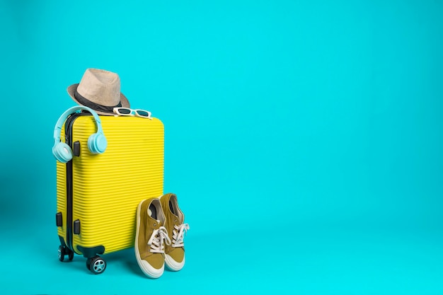 Yellow suitcase with sun glasses hat and camera on pastel blue background travel concept