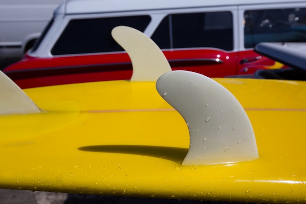 Le alette gialle della chiglia di tavola da surf dettagliano la retro automobile rossa di eith in california