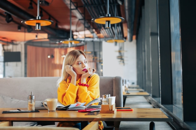 Maglione giallo bella donna elegante che indossa un maglione giallo e un braccialetto rosso che guarda nella finestra