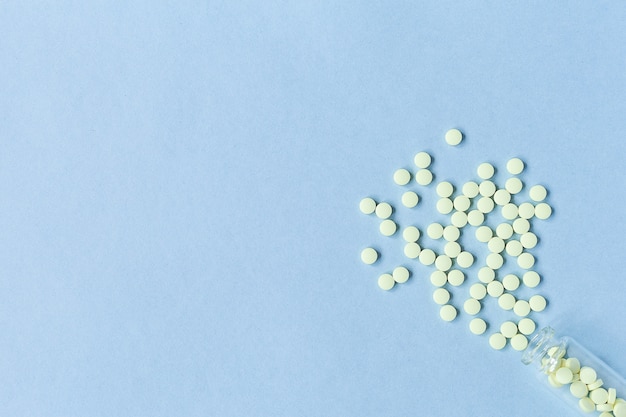 Yellow tablets are poured out of a glass bottle on a pastel blue background