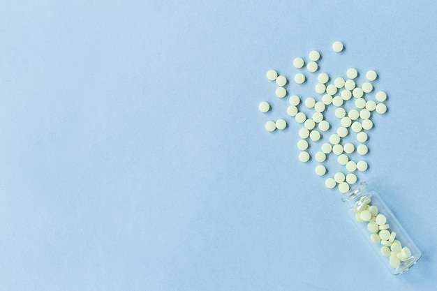 Yellow tablets are poured out of a glass bottle on a pastel blue background