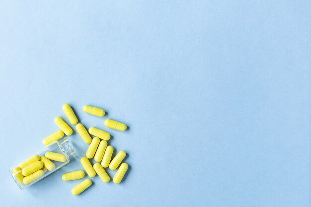 Photo yellow tablets are poured out of a glass bottle on a pastel blue background