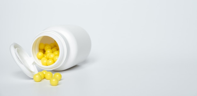 Yellow tablets of ascorbic acid in jar and lie on a white table.