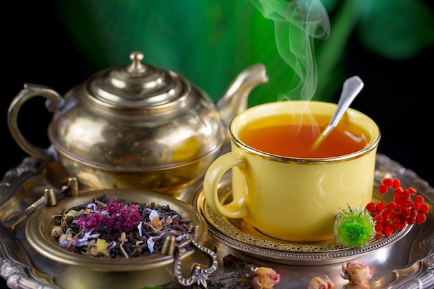 A yellow tea cup and a cup of tea with a teapot in the background.