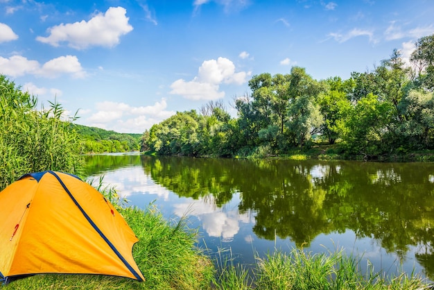 Yellow touristic tent near forest river in summer day