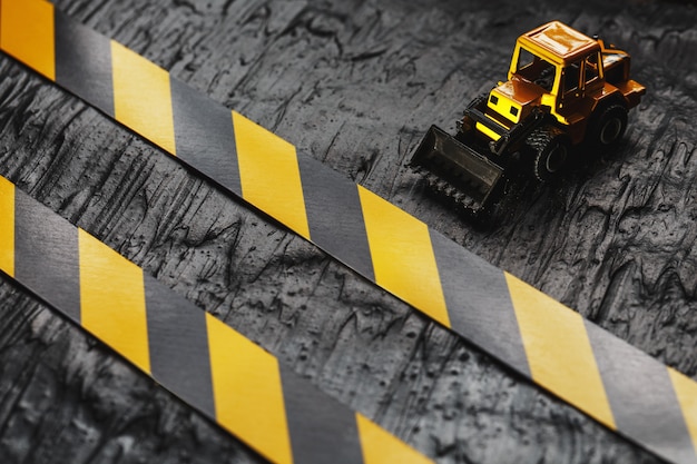 Yellow toy bulldozer. Black and yellow fence tape