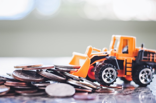 The yellow toy bulldozer with pile of coins against blurred background for saving money concept