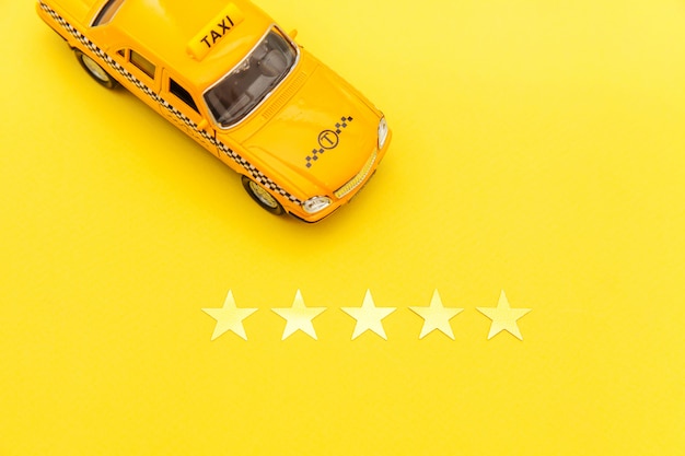 Carrozza di taxi gialla dell'automobile del giocattolo e una valutazione di 5 stelle isolata su fondo giallo. applicazione del telefono del servizio taxi per la ricerca online di chiamata e prenotazione concetto di cabina. simbolo taxi. copia spazio.