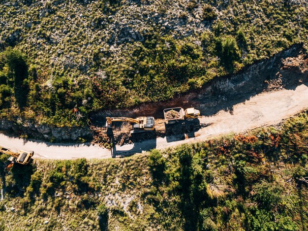 Il trattore cingolato giallo carica un veicolo da cava con vista sulla sabbia dall'alto