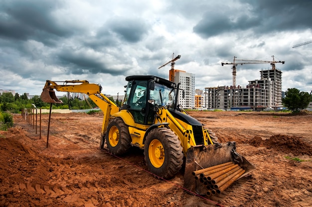 Желтый трактор на строительной площадке устанавливает столбы в поле