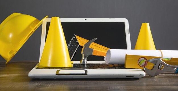 Yellow traffic cone helmet document hammer wrench with a laptop Under construction