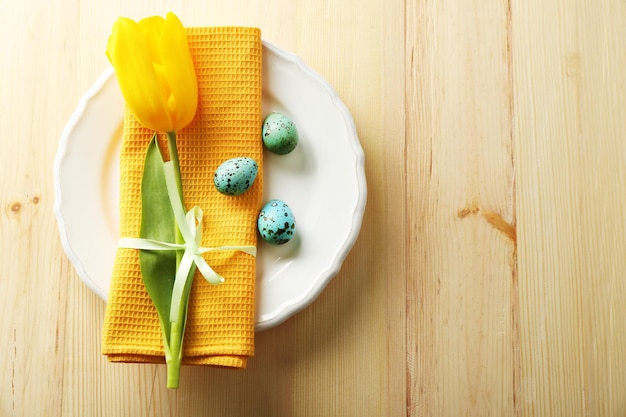 Yellow tulip colorful eggs and napkin on plate on wooden background