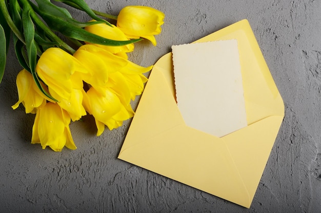 Yellow tulip near blank greeting card and envelope on grey background with space for text