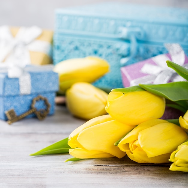 Yellow tulips in a blue metal box and gift boxes on the light gray surface. Greeting card for mother's day. Copy space