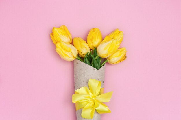 Yellow tulips in  craft paper with ribbon. Bright spring blooming flowers with copy space.  Flat lay.