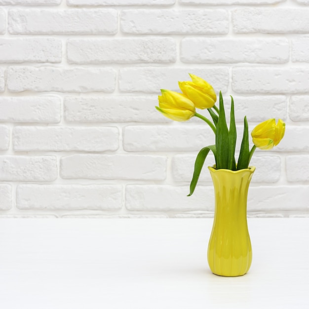 꽃병에 노란색 튤립입니다. 흰색 장식 벽돌 벽에 밝은 봄 개화 꽃.