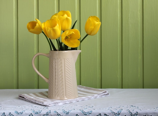 Tulipani gialli in una brocca su uno sfondo di bordo verde