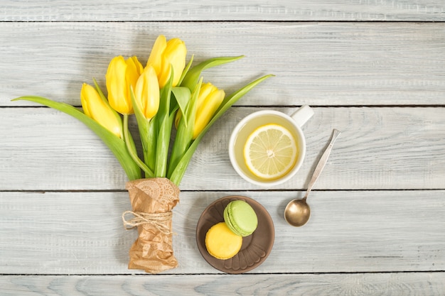 Желтые тюльпаны, чай с лимоном и макароны на белом деревянном столе
