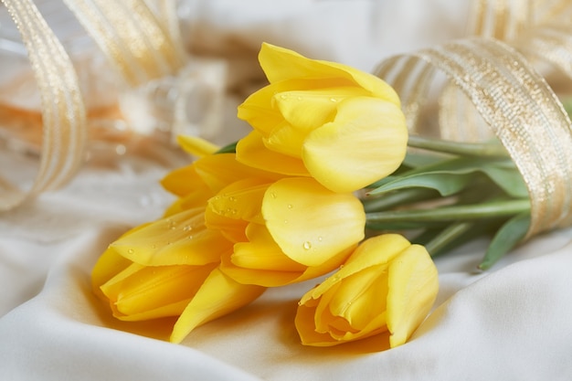 Yellow tulips, perfume and gold ribbon on silk linen