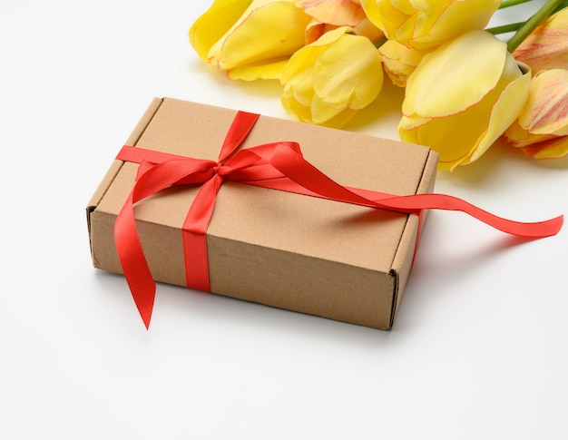 Yellow tulips and square box tied with red ribbon on white surface, festive surface for mother's day, birthday