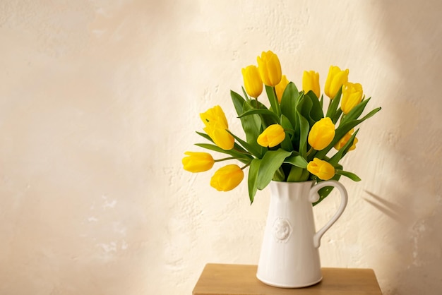 Yellow tulips in a white vase against a light wall Sunny photo with a bouquet of flowers and space for text