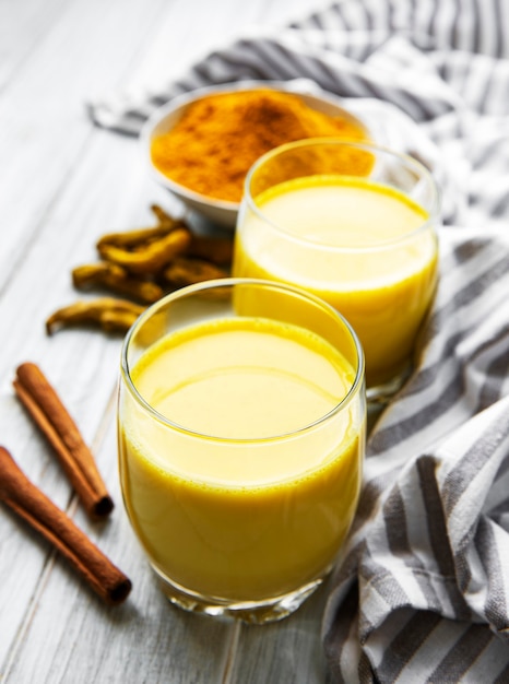 Yellow turmeric latte drink. Golden milk with cinnamon, turmeric, ginger  and honey over white marble table.