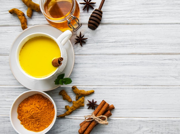 Yellow turmeric latte drink. Golden milk with cinnamon, turmeric, ginger  and honey over white wooden surface.