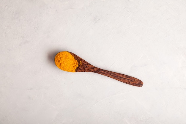 Yellow turmeric powder in wooden spoon on light background Top view copy space