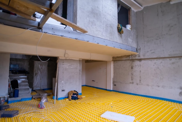 установка желтого теплого пола с белыми полиэтиленовыми трубами на строительной площадке новой двухуровневой квартиры