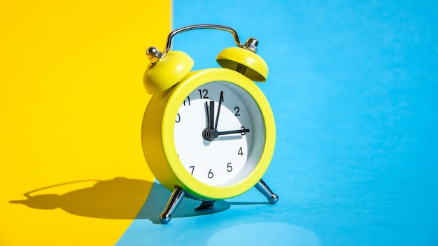 Yellow vintage alarm clock on a blue and yellow background with selective focus, copy space for text