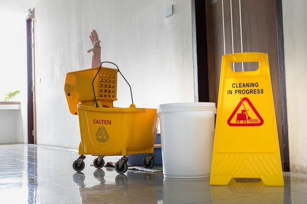 Yellow warning sign with message Cleaning in progress with cleaning trolley background