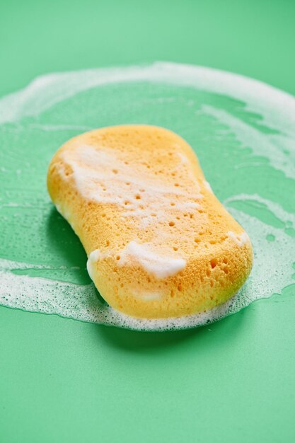 Yellow washing sponge in soap foam on a green background close up isolated