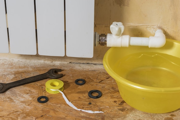 A yellow water basin and a set of tools near a leaking radiator. Accident of the heating system of a private house. Heating radiator.