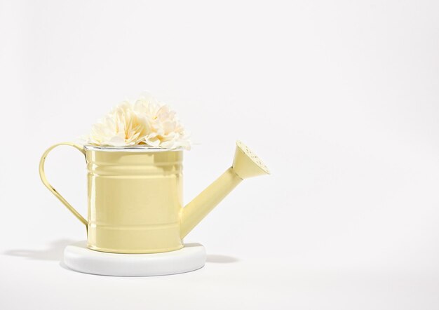 Yellow watering can for watering plants with flowers on a white round stand Copy space for text Garden works