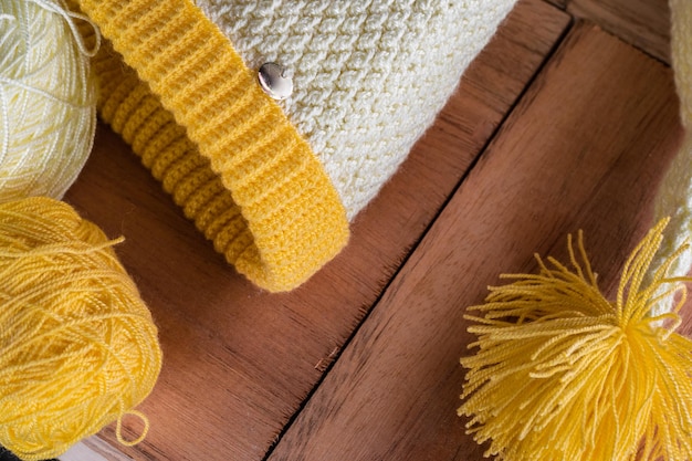 オレンジ色の木製の背景にかぎ針編みの技法で編まれた冬の手の黄色と白のキャップ