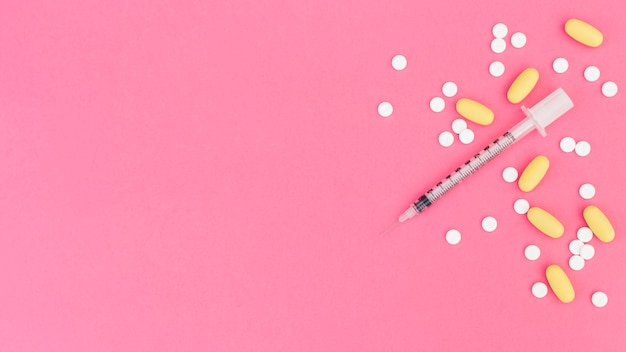 Photo yellow and white pills with syringe on pink background