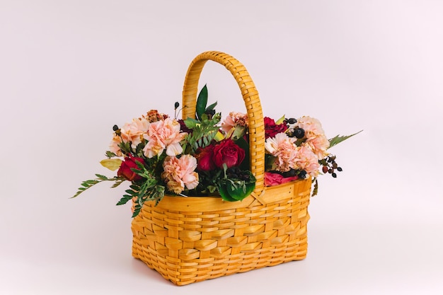 A yellow wicker basket with a bouquet of flowers stands on a delicate pink background