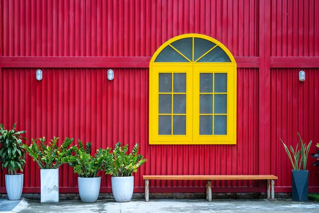 Yellow window flowerpots with plants and bench on the background of a red metal wall on the street of Danang city in Vietnam