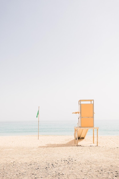 Yellow wooden rescue tower at the sand beach on a sunny summer day during Sea sky and green swimming flag background Lifeguard station Copy space Vacation concept