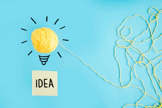 Photo yellow wool idea light bulb on blue background with idea text on sticky note