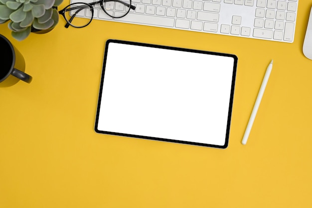 Yellow workspace tabletop with accessories and tablet white screen mockup top view