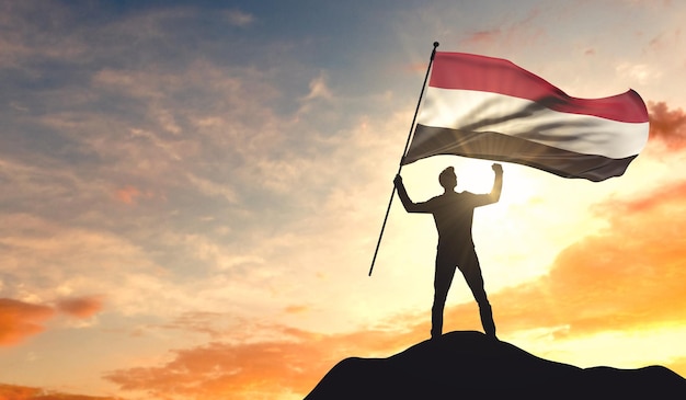 Yemen flag being waved by a man celebrating success at the top of a mountain 3D Rendering