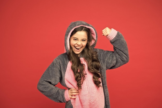 Yes I can Gorgeous girl in bunny costume Child in rabbit kigurumi Happy girl in bunny pajamas Lifestyle concept Rest and relax Cute bunny kid on red background Baby animal character role