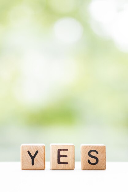 YES word is written on wooden cubes on a green summer background Closeup of wooden elements