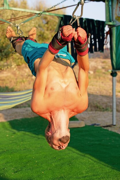 Yoga behandeling voor core, yoga swing, slanke jongeman vastgebonden aan vier planken boven de grond, man ontwikkelt uithoudingsvermogen en strekt zich uit.